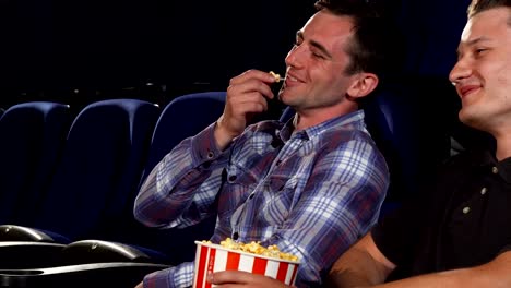 Male-friends-eating-popcorn-and-laughing-while-watching-comedies-at-the-cinema