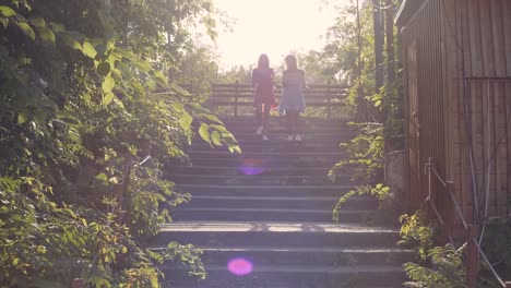 Two-attractive-beautiful-young-blond-women-blow-bubbles-in-the-park-and-are-happy-on-sunset.-Girlfriends-in-park-on-the-steps