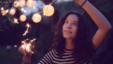 Slow-Motion-Aufnahme-junge-Frau-Beleuchtung-Wunderkerzen-im-Garten