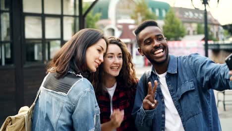 Gut-aussehende-junge-Menschen-kaukasischen-und-afrikanischen-amerikanischen-Touristen-nehmen-Selfie-mit-Smartphone-posiert-mit-Handgesten,-die-Spaß-am-Sommertag.