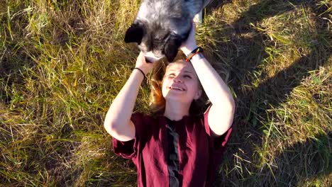 Top-view-of-young-girl-with-blonde-hair-lying-on-grass-at-field-and-stroking-her-husky-dog.-Beautiful-woman-spending-time-together-with-her-pet-at-nature.-Love-and-friendship-with-domestic-animal.