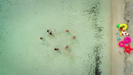 Aerial-view-of-friends-playing-volleyball-standing-in-sea-by-sandy-beach.