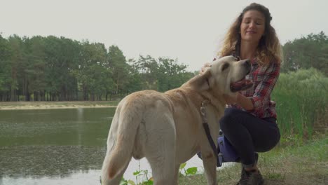 Chica-joven-pelirroja-está-acariciando-a-su-perro-cerca-del-río