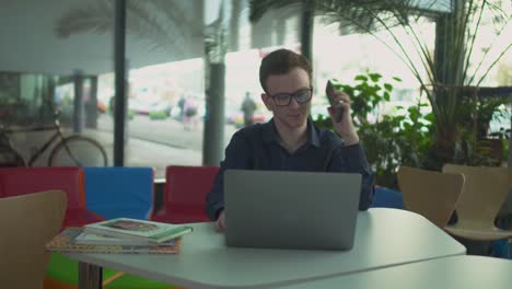 The-guy-in-the-glasses-talking-on-the-phone-while-sitting-at-a-laptop