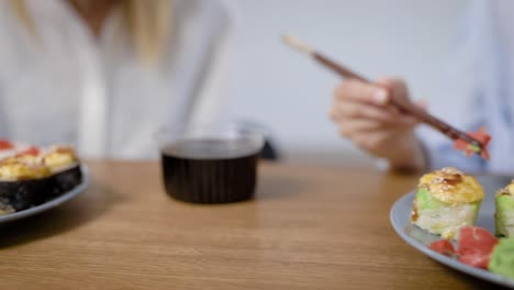 Two-beautiful-girls-eat-Japanese-food-at-home.-Rolls-on-a-plate-are-different,-very-tasty