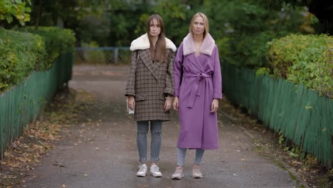 Two-beautiful-women-posing-outdoor-in-autumn,-standing-still-in-stylish-clothes