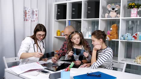 Female-doctor-talking-with-the-father-of-two-daughters,-and-shows-him-x-ray.-youngest-daughter.