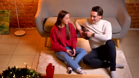 Close-up-top-down-view-of-talking-young-caucasian-friends-sitting-on-carpet-with-wine-in-cosy-home-christmas-atmosphere.