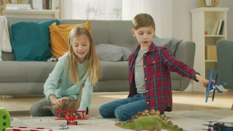 Im-Wohnzimmer:-jungen-und-Mädchen-spielen-mit-Spielzeug-Flugzeuge-und-Dinosaurier-beim-Sitzen-auf-einem-Teppich.-Helles-Wohnzimmer-mit-Kindern-Spaß.