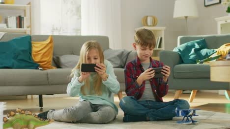 Zu-Hause-auf-einem-Teppich-sitzen:-niedliche-kleine-Mädchen-und-süße-junge-Videospiel-in-wettbewerbsfähige-auf-zwei-Smartphones,-hielt-sie-im-horizontalen-Modus-\"Querformat\".-In-Zeitlupe.