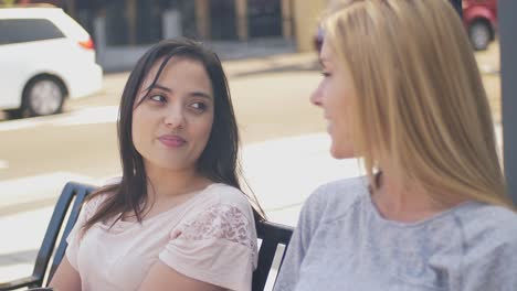 Two-friends-sitting-on-a-bench-in-a-city-and-talking