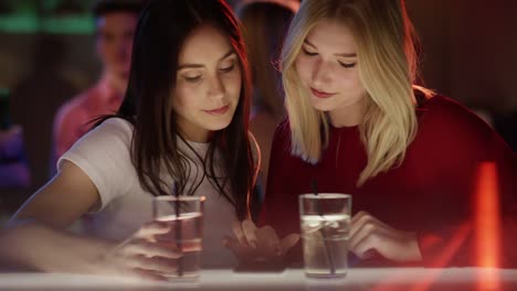 Las-chicas-en-el-bar-observando-a-teléfono-inteligente