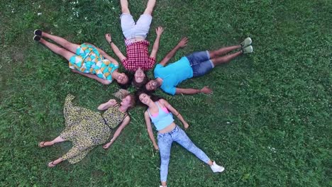 Young-friends-forming-a-star-shape-lying-in-grass-and-waving-to-camera