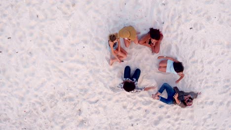 Multi-Ethnic-Hipster-Friends-sitting-on-Sandy-Beach-and-hug-each-other