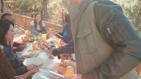 Hombre-joven-sirve-a-amigos-en-una-mesa-de-comida-de-barbacoa