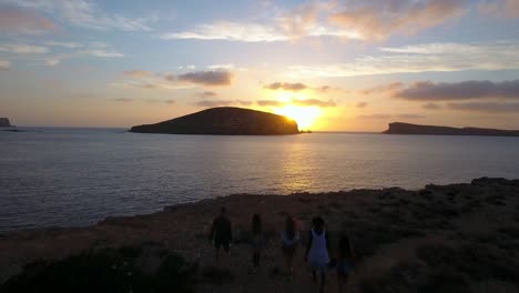 Toma-aérea-de-amigos-en-acantilados-mirando-sol-conjunto-sobre-mar