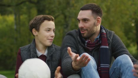 Padre-e-hijo-hablando-en-el-parque.-Hijo-tiene-bola.