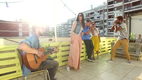 Freunde,-die-Spaß-auf-der-Dachterrasse-haben,-Gitarre-spielen-und-Fotos-machen