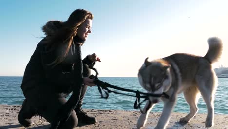 Mujer-joven-divirtiéndose-con-el-perro-husky-siberiano-en-el-muelle-del-mar