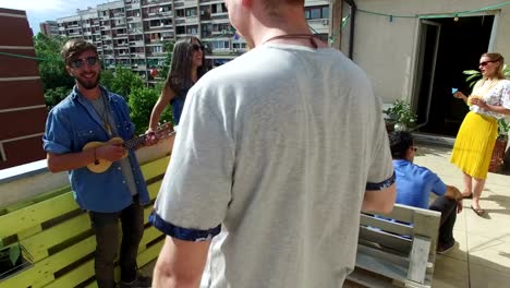 Man-playing-ukulele-while-hanging-out-with-friends-on-the-rooftop