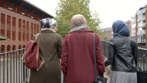 Rear-View-Of-British-Muslim-Female-Friends-Walking-In-City