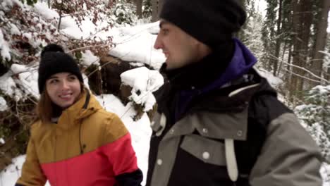 Young-man-and-woman-in-winter-clothing-walk-together-holding-hands-in-winter-forest.