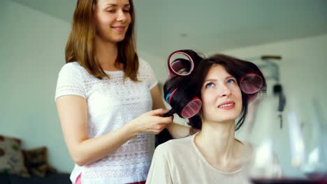 Two-happy-women-friends-make-fun-curler-hairstyle-each-other-and-have-fun-at-home