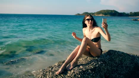 Young-happy-woman-chatting-with-friends-through-internet-using-smartphone-in-ocean-beach