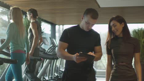 Hombre-y-mujer-atléticas-están-usando-una-tableta-junto-a-las-cintas-de-correr-en-un-gimnasio-deportivo.