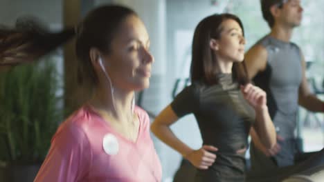 Slow-motion-footage-of-attractive-caucasian-girl-running-on-the-treadmill-in-the-sport-gym-with-earphones.