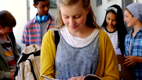 Portrait-of-smiling-schoolgirl-standing-with-notebook-in-corridor