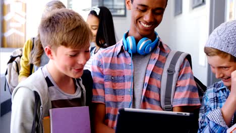 Students-standing-with-notebook-and-digital-tablet-in-corridor