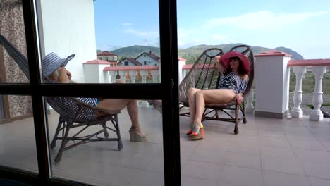 Two-women-relaxing-in-cane-chairs-on-open-terrace-balcony-at-vacation-home