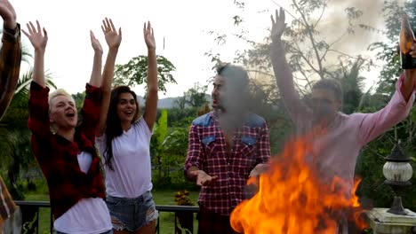 Gente-joven-alegre-cocina-barbacoa-feliz-grupo-de-amigos-elevar-manos-reunión-en-terraza-de-verano-fiesta