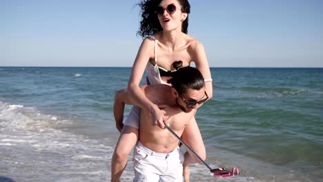 mobile-phone-on-Selfi-stick,-positive-young-people-shoot-video-from-holiday-travel,-love-couple-make-Selfi-photo-on-beach