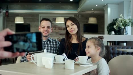 Someone-taking-photo-on-cell-phone-of-young-happy-family-in-cafe