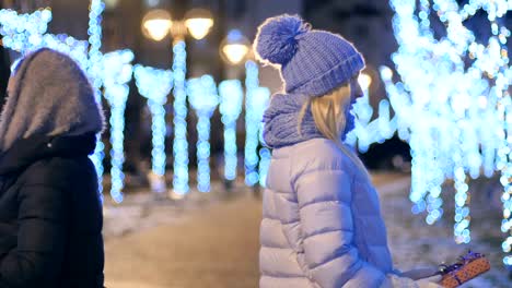 Zwei-Mädchen-gibt-einen-Geschenke-zueinander-bei-Nacht-Lichter-Hintergrund