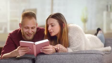 Pareja-dulce-joven-tumbado-en-un-sillón-y-leer-un-libro-divertido