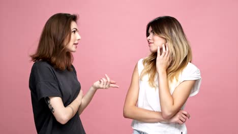 Young-pretty-girl-suggesting-ideas-to-her-doubting-unsure-female-friend-isolated-over-pink-background