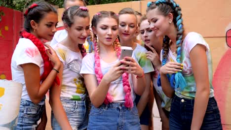 crowd-of-girls-with-bright-braids-with-gadget-in-arms-on-open-air,-Laughing-team-of-youth-Looks-at-photos-on-phone