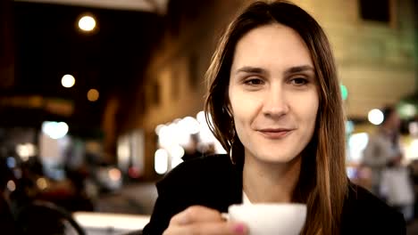 Young-happy-woman-talking-with-friend,-sitting-in-cafe-in-the-evening-and-drinking-coffee-in-the-city-centre