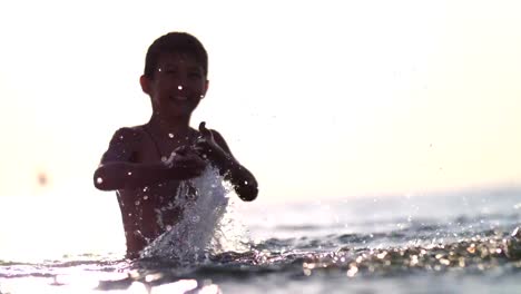 Jungen-spielen-mit-Wasser-im-Meer-bei-Sonnenuntergang,-spritzt