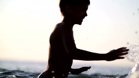 Jungen-spielen-mit-Wasser-im-Meer-bei-Sonnenuntergang,-spritzt