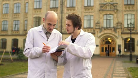 Two-medical-students-in-bathrobes-discuss-something-at-campus-background