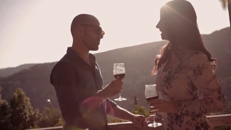 Pareja-joven/esposos-beber-vino-en-balcón-rústico-con-vistas-a-la-montaña