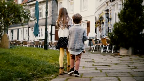 Two-little-kids-walk-together-near-old-buildings.-Children,-girl-and-boy-wander-around-beautiful-German-old-town.-4K