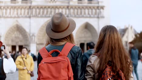 Back-view-of-two-traveling-woman-with-backpack-walking-near-the-Notre-Dame,-famous-cathedral-in-Paris,-France