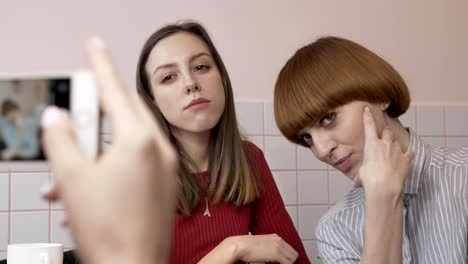 Joven-hermosa-chica-caucásica-está-haciendo-una-foto-en-el-teléfono-inteligente-de-sus-dos-amigas-sentadas-en-un-café.-Las-niñas-están-posando.-Amigas-en-el-café-concepto.-Con-un-smartphone-cerca-a-60-fps