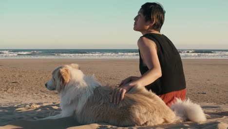 Frau-streicheln-ihren-Hund-am-Strand-bei-Sonnenuntergang