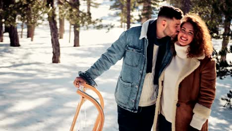 Joven-pareja-romántica-con-trineo-besos-en-la-nieve